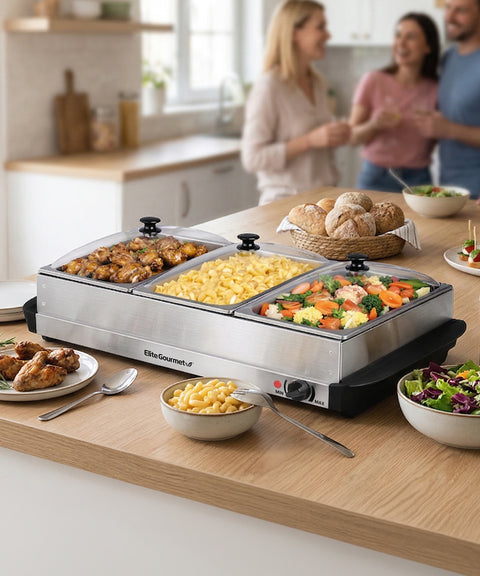 Buffet setup with food warmers and plates on a kitchen counter, with people in the background.