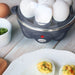 Egg cooker power indicator light is lit red.  Plate of deviled eggs next to egg cooker.