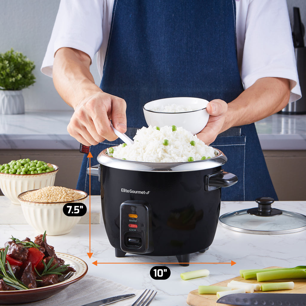 User scoops cooked rice into bowl.  Rice Cooker is set on kitchen counter next to vegetables, grains and other ingredients.