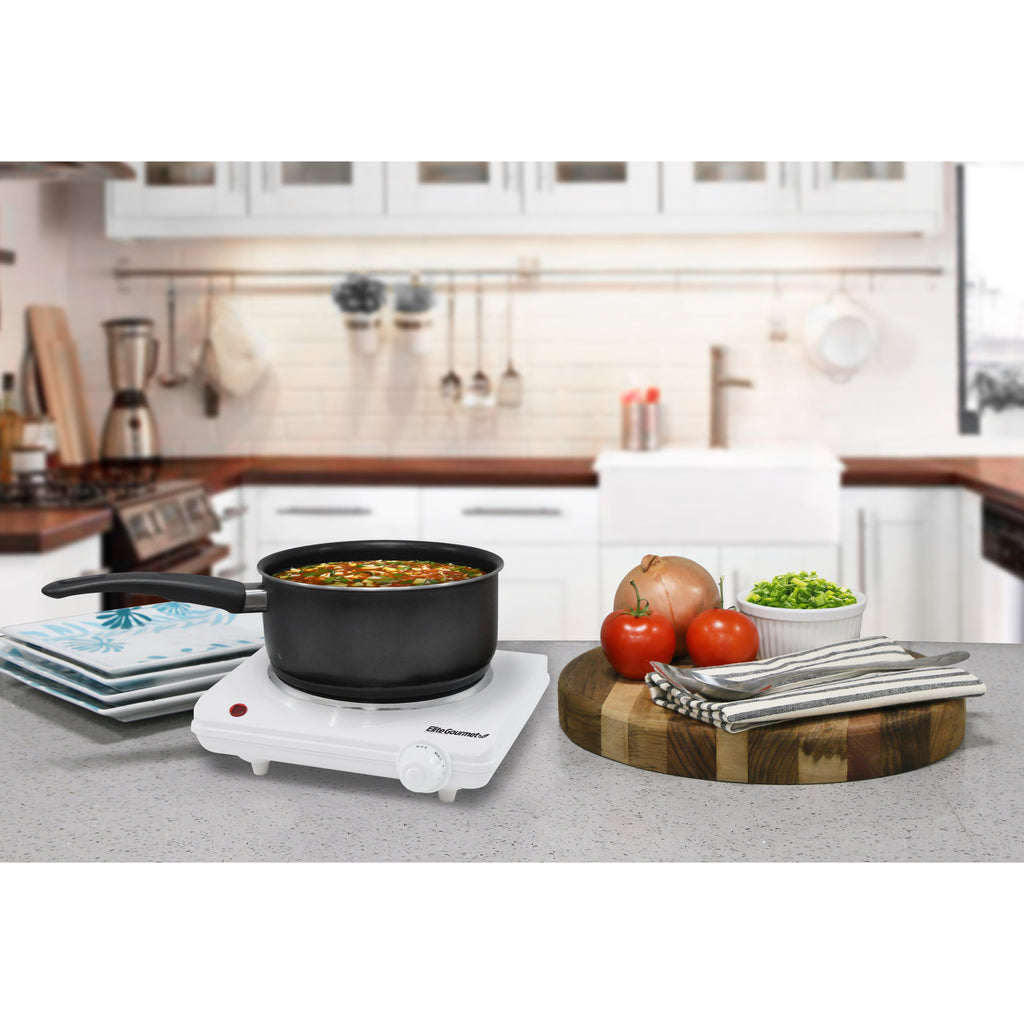 Flat Burner on kitchen counter with saucepan cooking soup.  Next to various serving plates, cutting board and ingredients.